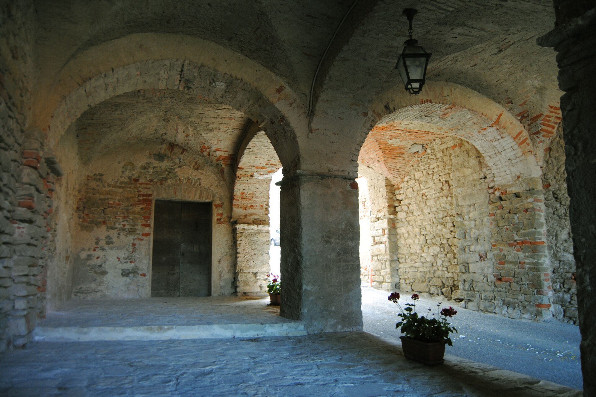 Pórticos de pedra e tijolos em Cravanzana, com arcos, uma porta e vasos de flores