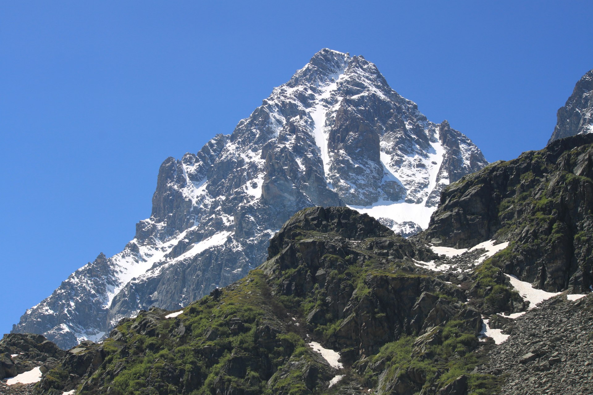 Pico rochoso do Monviso com neve e encostas verdes sob céu azul