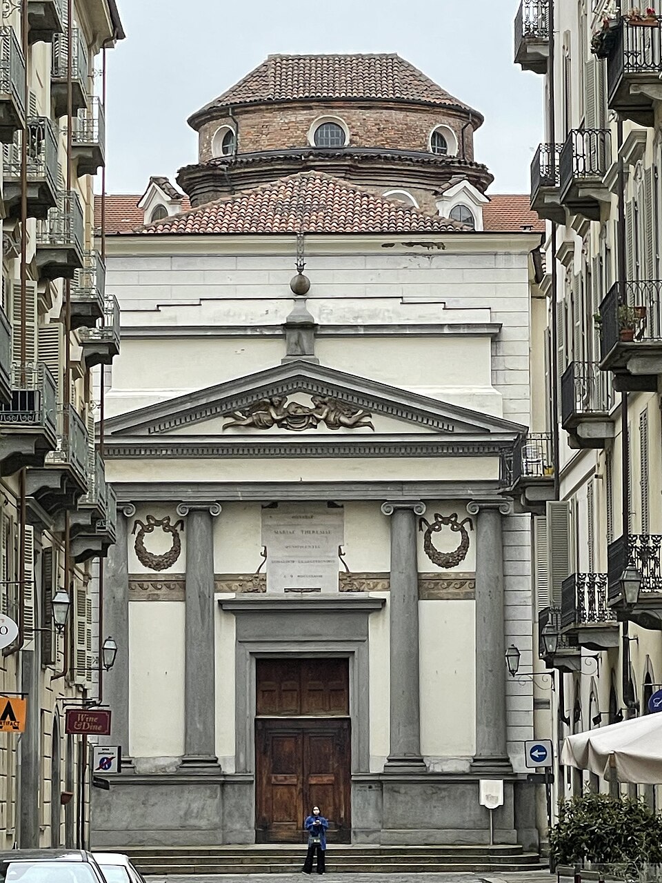 Fachada clara da Chiesa della Misericordia, com quatro colunas e frontão triangular, entre edifícios do centro de Turim.