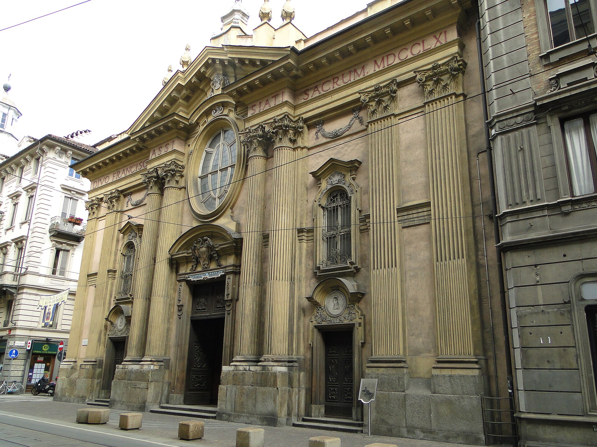 Fachada da igreja San Francesco d’Assisi em Turim, vista de baixo, com colunas, janela oval e portais de madeira.