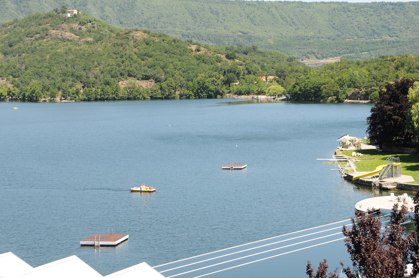 Lago Sirio cercado por colinas verdes, com pequenos barcos junto à margem