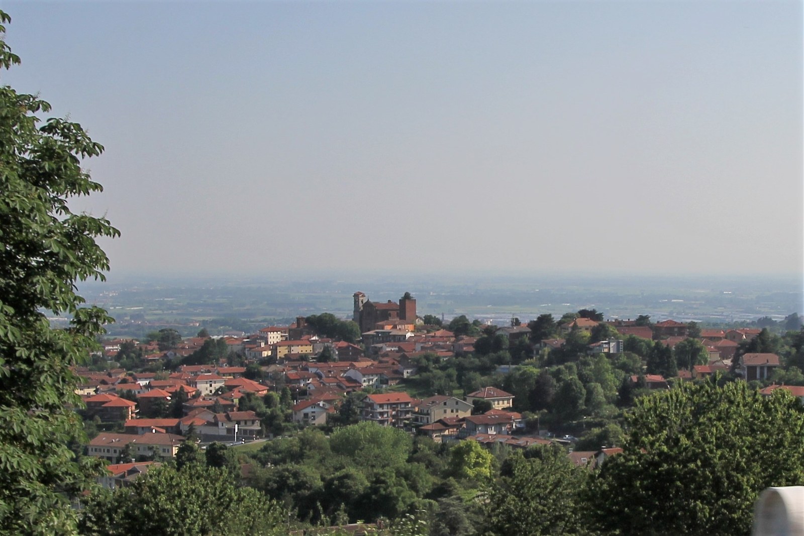 Casas e torre de Pecetto Torinese entre áreas verdes, com a planície ao fundo