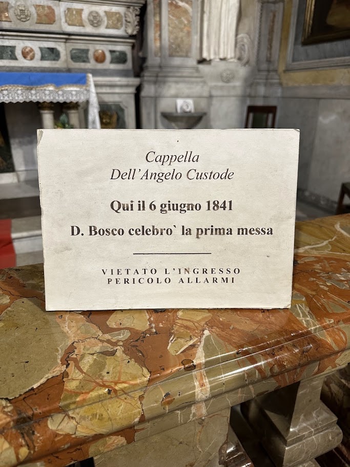 Placa sobre uma balaustrada de mármore com a inscrição de que Dom Bosco celebrou ali sua primeira missa em 6 de junho de 1841
