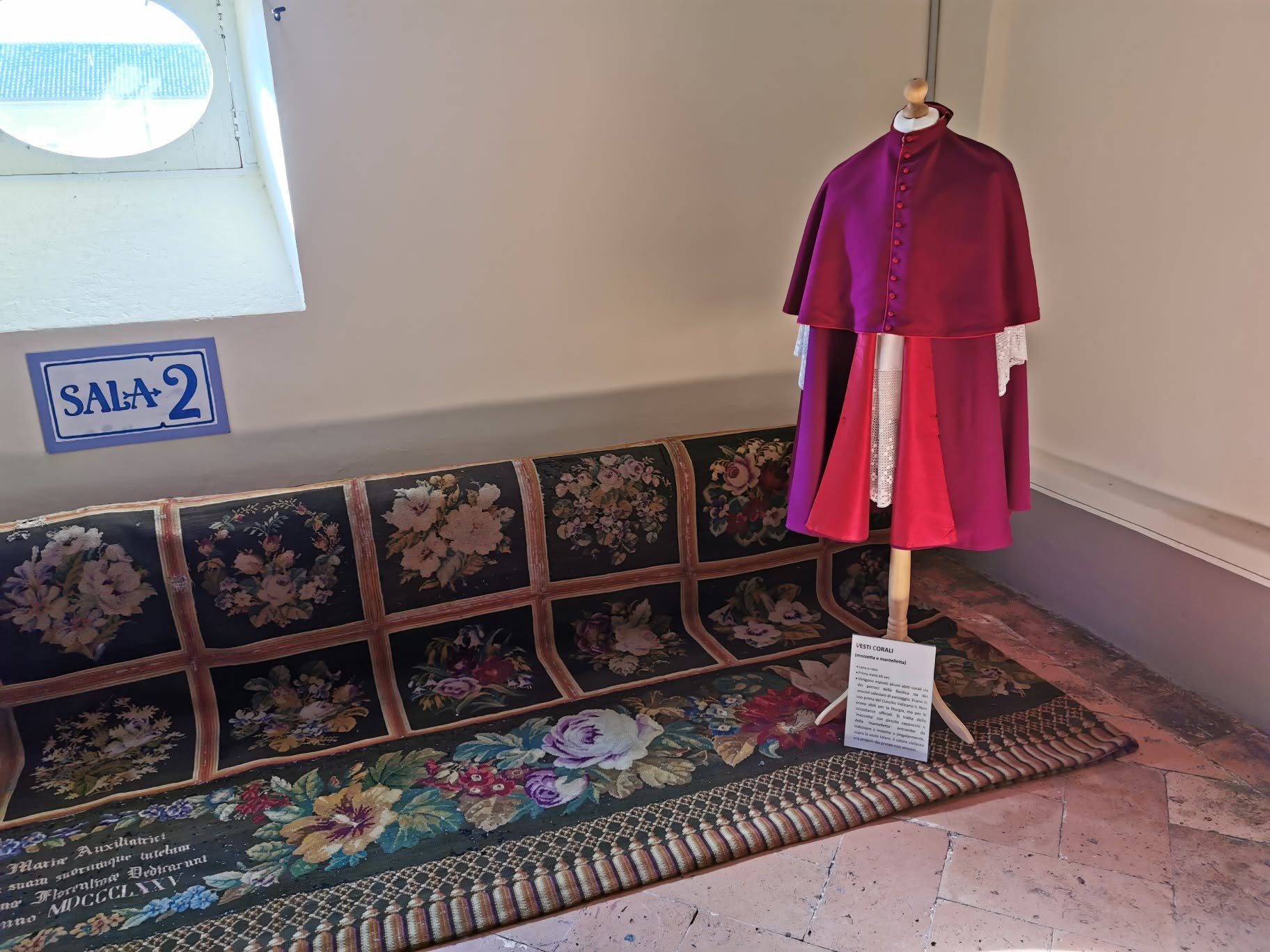 Vestes corais expostas ao lado do tapete policromado oferecido a Dom Bosco