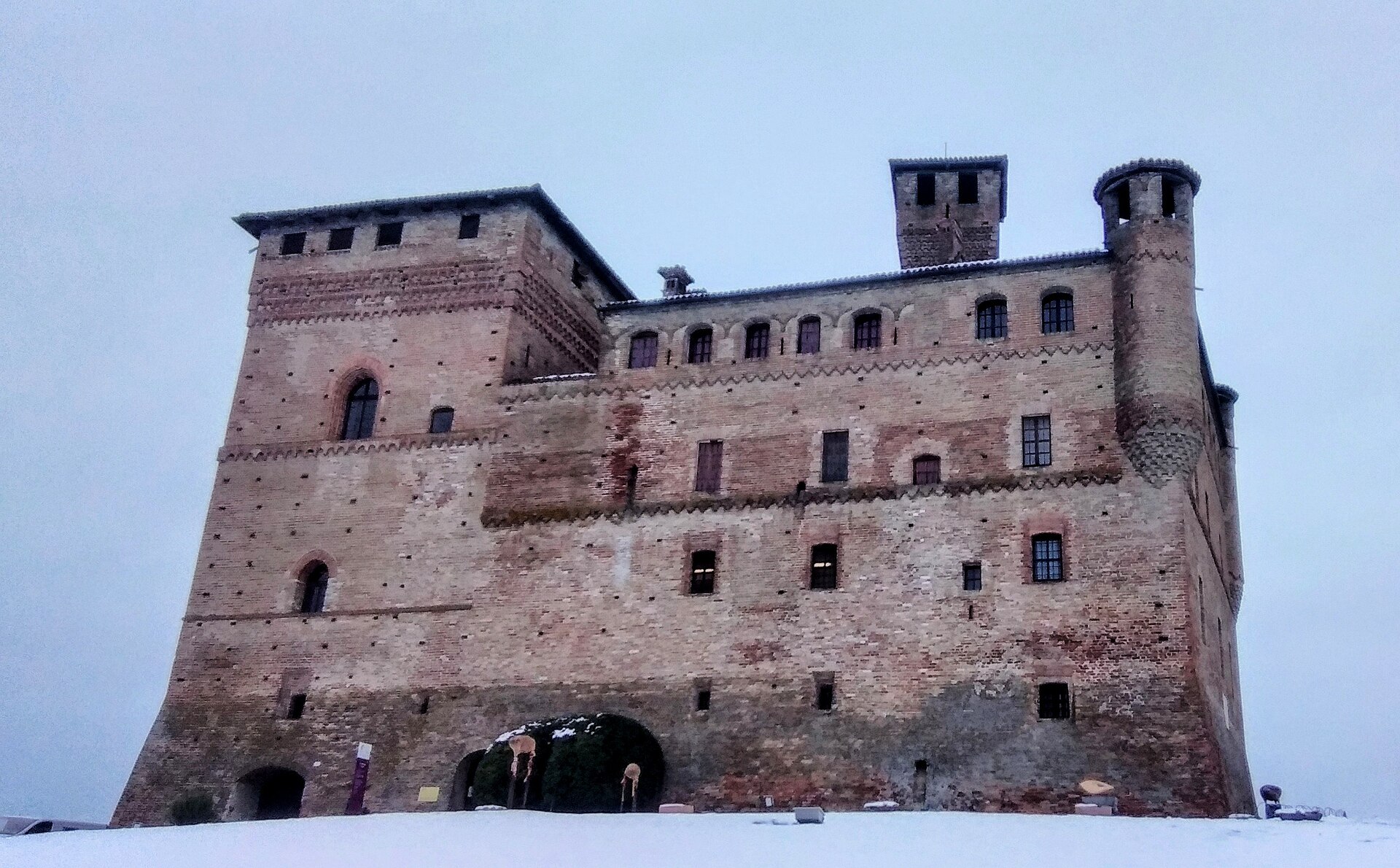 Castelo de Grinzane Cavour com fachada de tijolos, torres e neve no solo