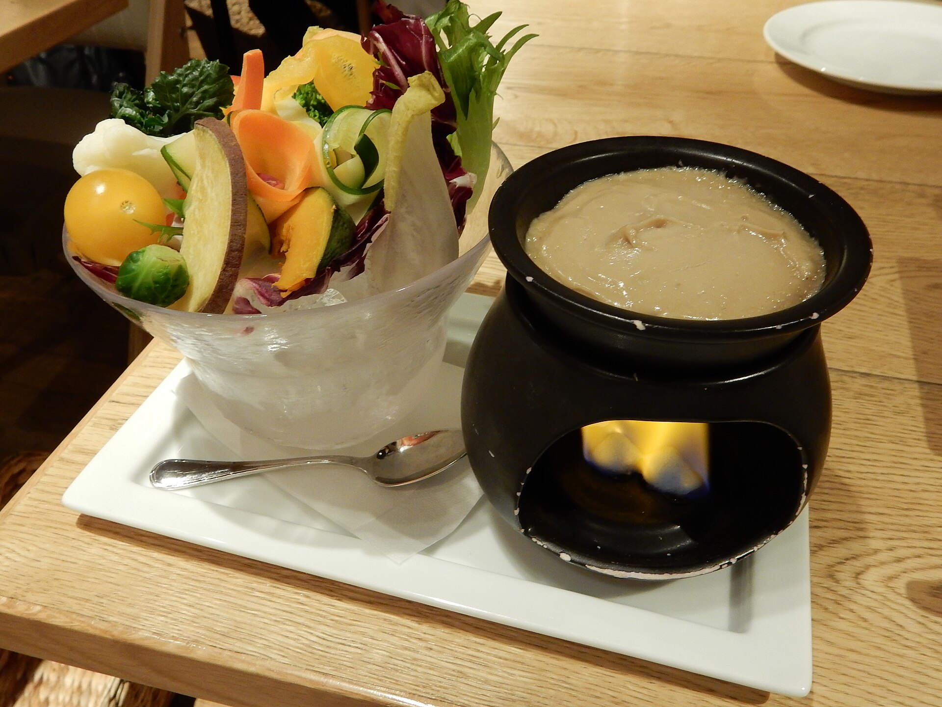 Recipiente aquecido de bagna cauda ao lado de uma tigela com verduras