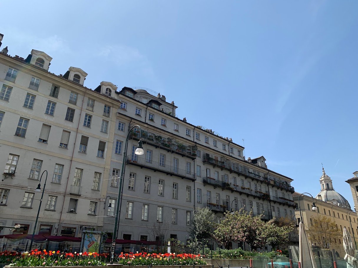 Praça com tulipas, fachadas e uma cúpula sob o céu azul em Turim