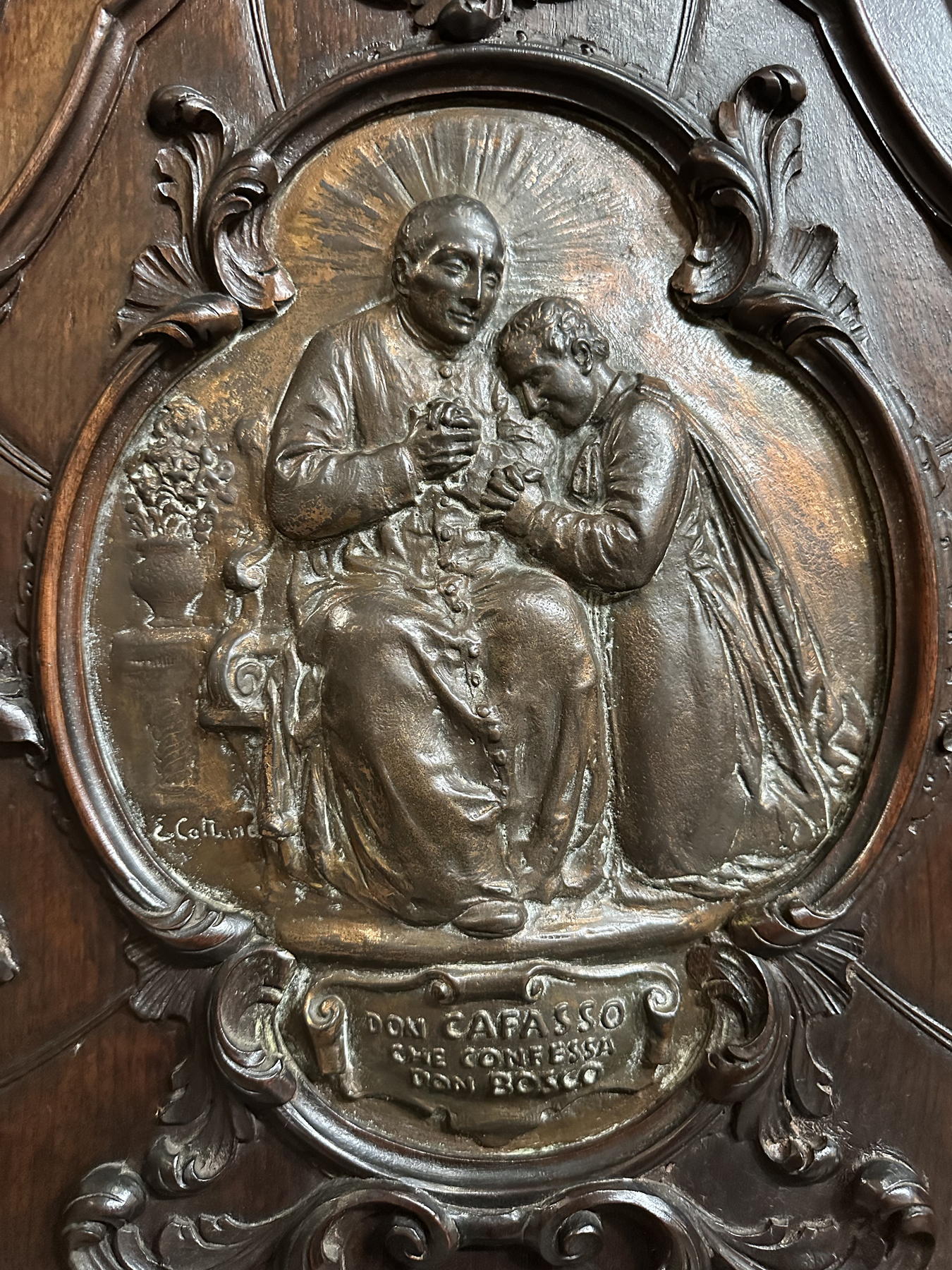 Relevo de São José Cafasso com Dom Bosco, sinal de sua presença como mestre, confessor e orientador espiritual.