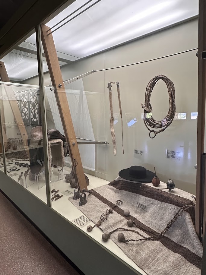 Tecidos, chapéu e cordas em uma vitrine do museu