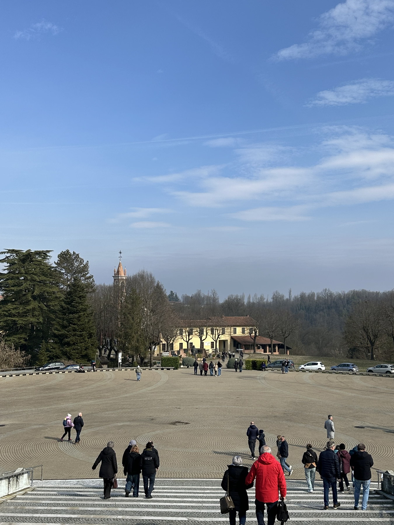 Visitantes nos espaços abertos do Colle Don Bosco, com colinas e vegetação ao fundo