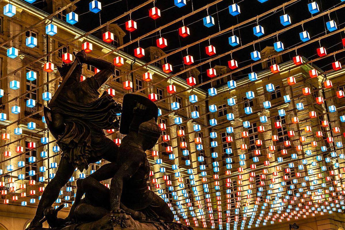 Cubos luminosos coloridos suspensos sobre uma praça à noite