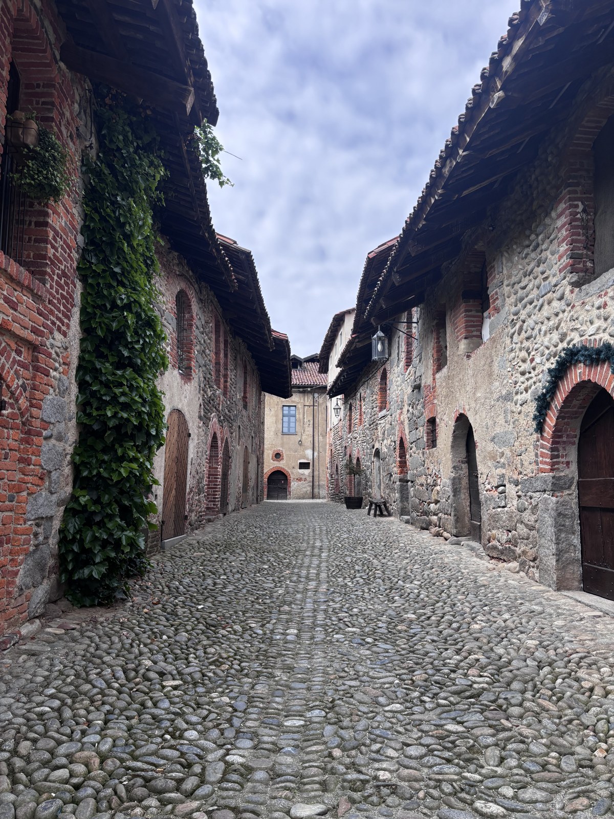 Rua de pedras do Ricetto di Candelo entre construções de tijolos e seixos, com portas e pequenos balcões