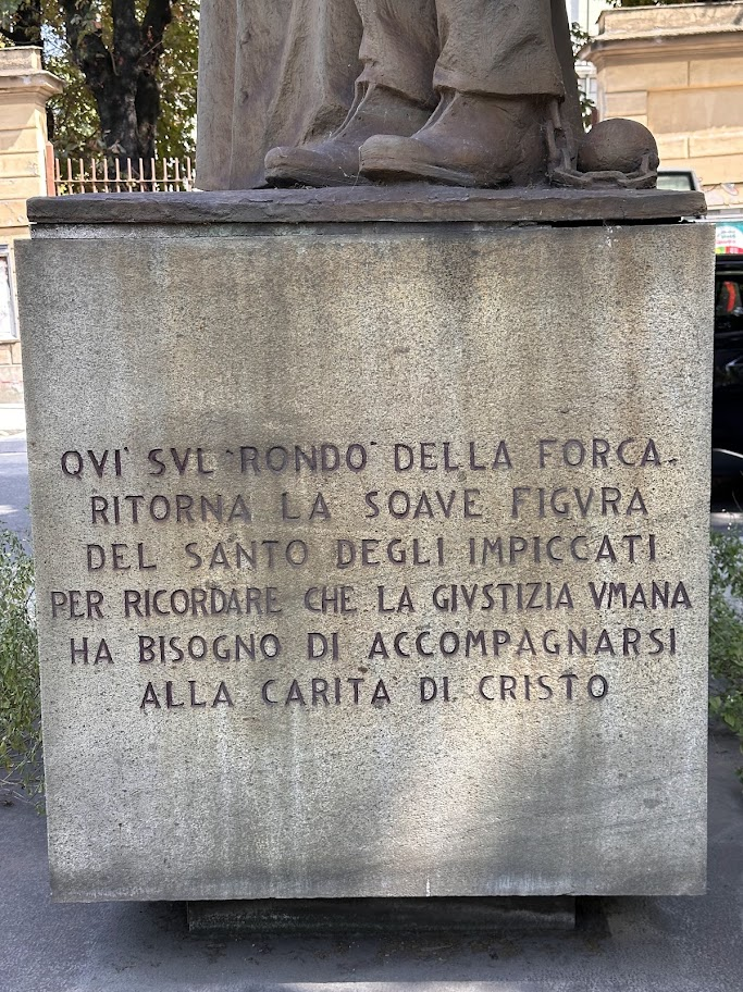 Detalhe do pedestal de pedra do monumento a Giuseppe Cafasso, com a inscrição italiana sobre a justiça humana e a caridade de Cristo.