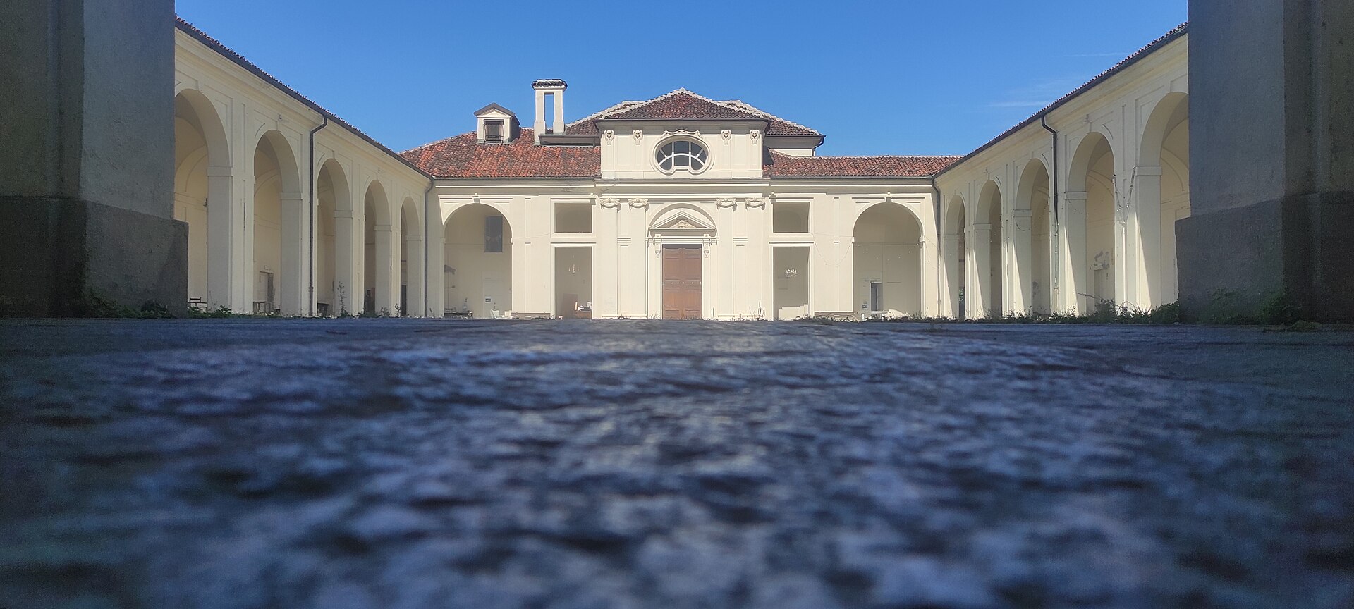 Pátio do antigo cemitério de San Pietro in Vincoli, com pavimento em primeiro plano, pórticos laterais e capela clara ao fundo.