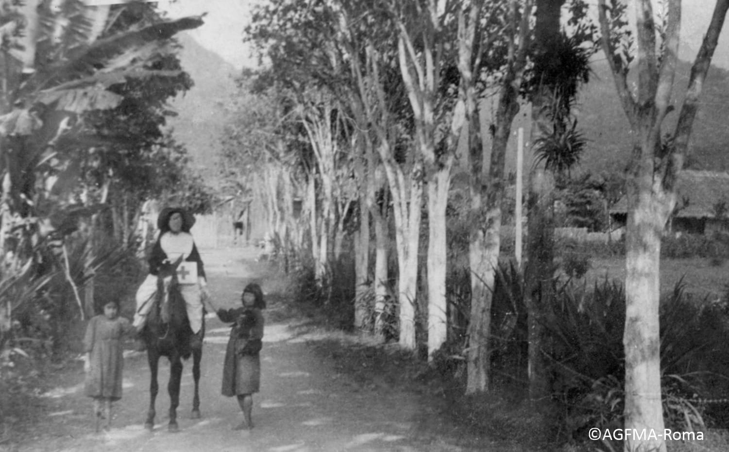 Maria Troncatti a cavalo em um caminho arborizado, acompanhada por duas meninas a pé