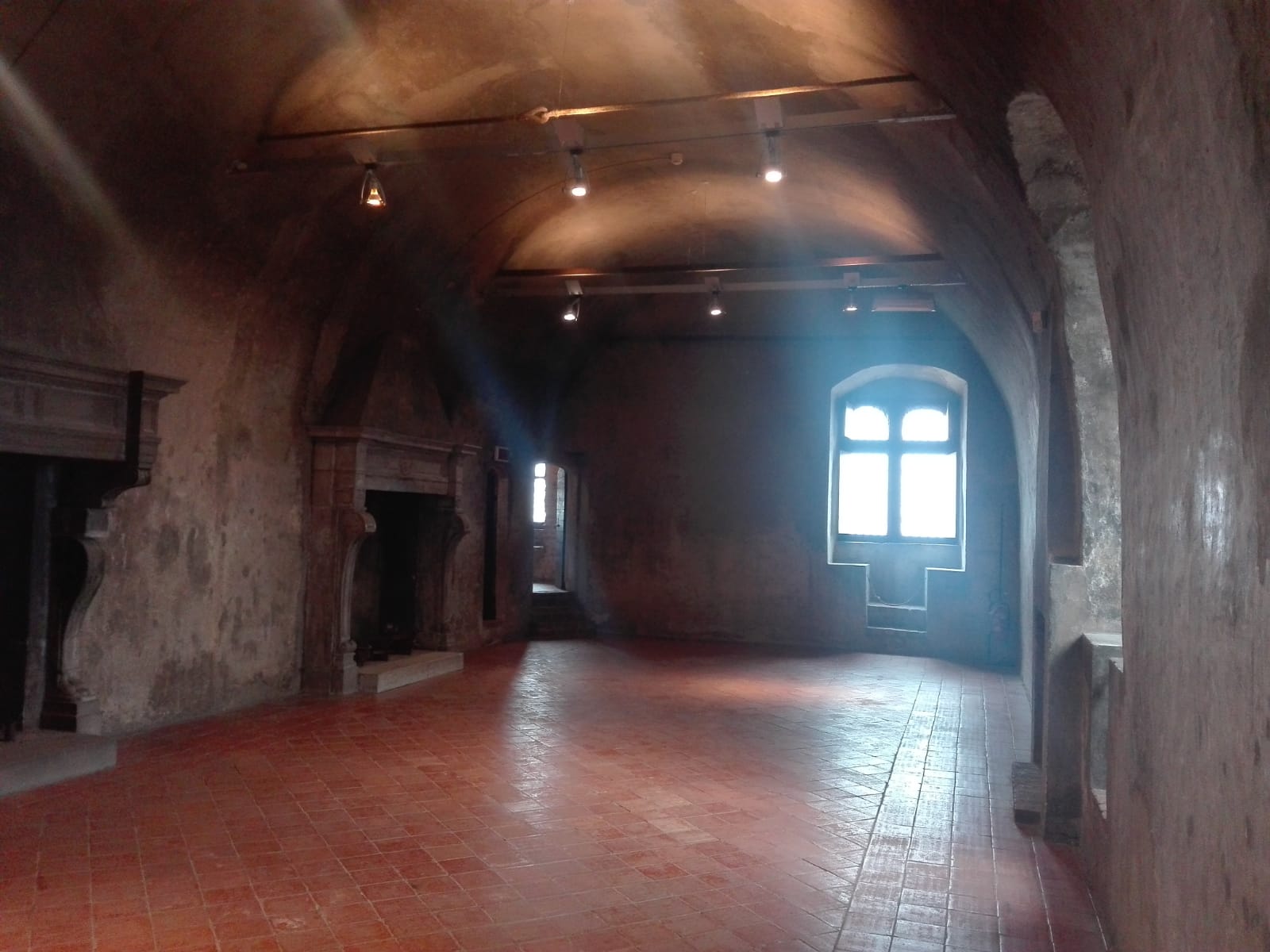 Sala do castelo de Serralunga com lareiras, piso de tijolos e uma janela iluminada