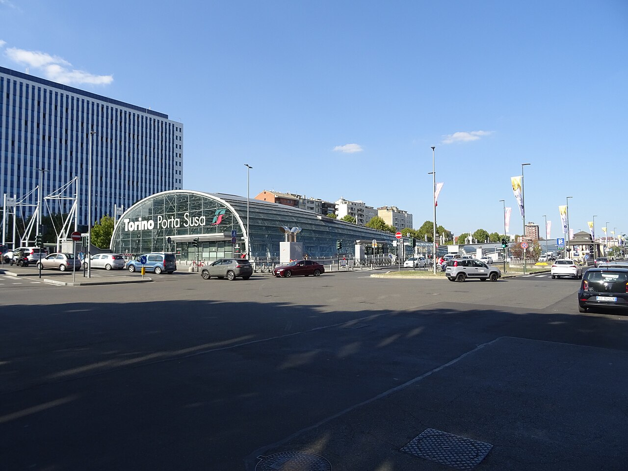 Estação Torino Porta Susa, com cobertura curva de vidro e o nome na fachada, vista do outro lado da rua