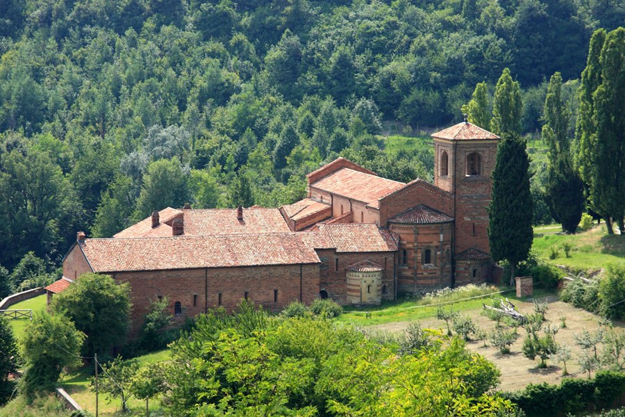 Complexo de Santa Maria di Vezzolano com telhados de cerâmica, campanário e encosta arborizada